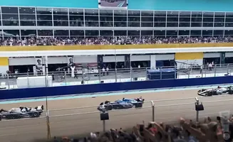 A race car speeds past a pit stop with spectators in the grandstands.
