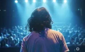 Person on stage facing a crowd, lit by blue stage lights.