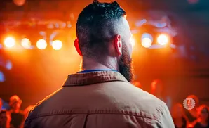 Man with beard faces away from camera, illuminated by orange stage lights.