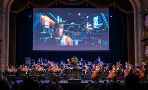 An orchestra performs live to a Star Wars movie projection on a large screen.
