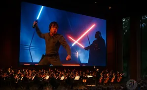 An orchestra plays live to a giant screen showing Luke Skywalker dueling Darth Vader with lightsabers.