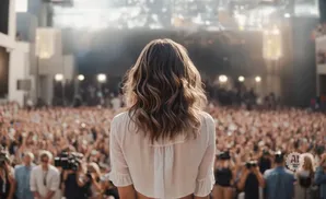 Woman in white shirt facing a large, cheering crowd at an outdoor concert venue.