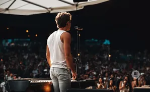 A singer on stage plays a piano in front of a large audience.