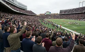 A crowded football stadium with fans in maroon and gold cheering on their team.