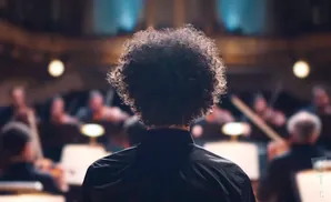 View from behind of a conductor with a large afro, leading an orchestra.