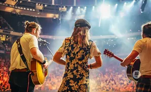 Three musicians perform on stage with guitars in front of a cheering crowd.