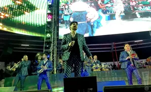 A band in matching sparkly suits performs on stage with a large screen behind them.