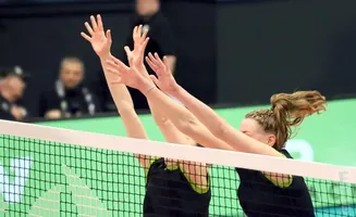 Two volleyball players jump to block at the net.