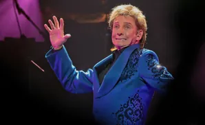 Singer Barry Manilow waves to the audience in a blue sequined jacket.