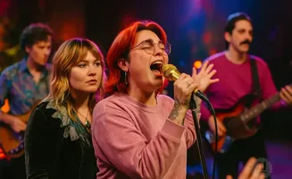 A band performs on stage with a female lead singer, a guitarist, and a bassist.