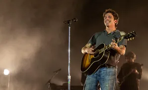 A man smiles and plays an acoustic guitar on stage.