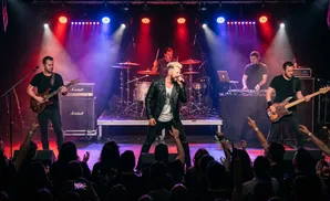 A band performs live on stage with colorful lights and a cheering audience.