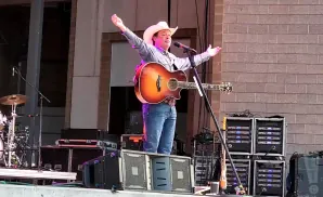 A country singer in a white cowboy hat performs with a guitar on stage.