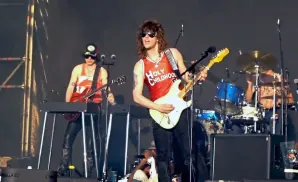 A band performs on stage, with two guitarists in the foreground and a drummer in the background.