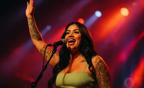 A tattooed woman sings into a microphone on a brightly lit stage.