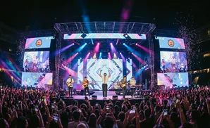 A young person in a denim jacket stands with their back to the camera, facing a blurred crowd.
