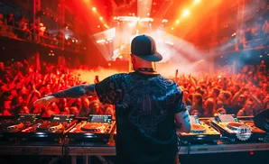 DJ performing for a large crowd at a concert with red stage lights.