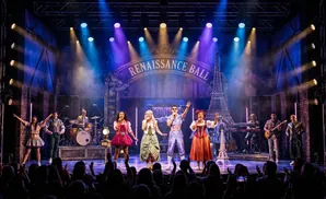 A stage musical performance with singers and musicians under colorful lights, with a 