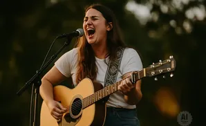 A woman sings and plays an acoustic guitar into a microphone.