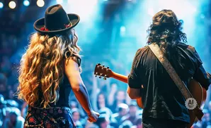A woman in a hat and a man with a guitar perform on stage.