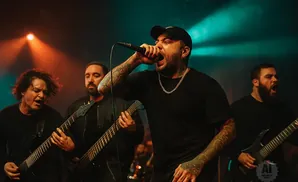 A band performs on stage with a singer at the microphone and guitarists playing.