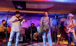 A country band plays on stage, with a violinist, guitarist, bassist, and drummer.