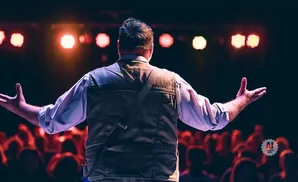 Man with arms outstretched on stage in front of a blurred audience.