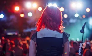 Woman with red hair faces away from camera at a concert, illuminated by stage lights.