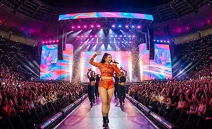 Singer Rosalía performs on stage with dancers at a concert in a stadium filled with cheering fans holding up lights.