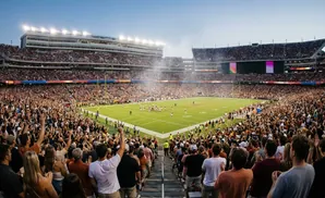 Football stadium packed with fans in orange and black attire, watching a game under stadium lights.