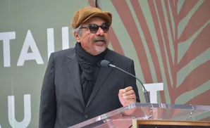 A man in a tan cap and sunglasses speaks at a podium.