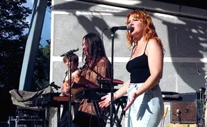 A band performs on an outdoor stage with a woman singing into a microphone.