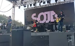 Band performing on stage with a large screen displaying 