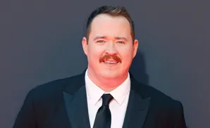 A man in a tuxedo with a mustache smiles at the camera.