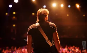 A musician with their back to the camera stands on stage, bathed in warm spotlight.