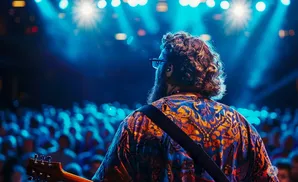 Guitarist performing on stage with a crowd and blue stage lights.