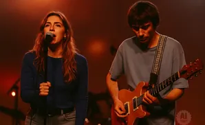 A female singer and a male guitarist perform on stage with warm lighting.