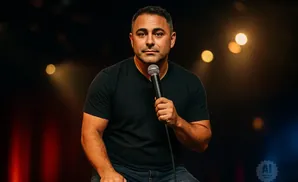 A man in a black t-shirt holds a microphone on a dimly lit stage.