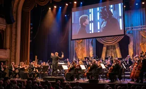 An orchestra plays in front of a screen showing Darth Vader and Luke Skywalker.