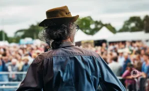 Man in a cowboy hat from behind, looking at a crowd at an outdoor event.