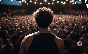 Rear view of a person with curly hair on stage facing a cheering, dimly lit crowd.