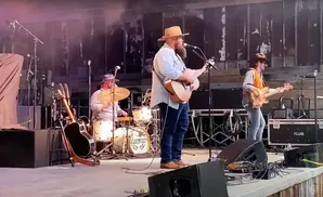 A band performs on stage, with a guitarist singing, a drummer playing, and a bassist.