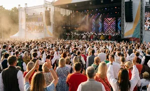 People in traditional outfits dance on stage at an outdoor festival.