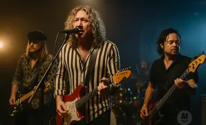 A band performs on stage with a lead singer playing a red guitar and a bassist on the right.