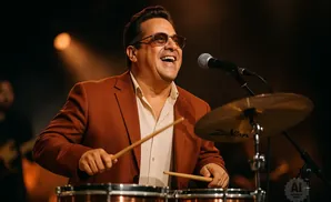 Man in a brown suit plays drums and sings into a microphone.