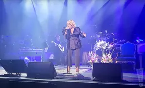 Patti LaBelle performs on stage with her band in a blue-lit venue.
