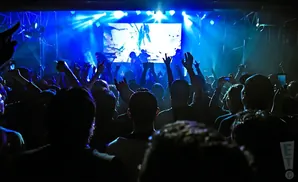 Crowd at a concert with blue stage lighting and a band on screen.