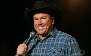 A man wearing a cowboy hat and a plaid shirt smiles while holding a microphone.