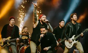 A band performs on stage with pyrotechnics, the lead singer holding his hand up in a rock-and-roll gesture.