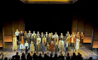 A large cast of actors, including children, stand on stage for a bow.